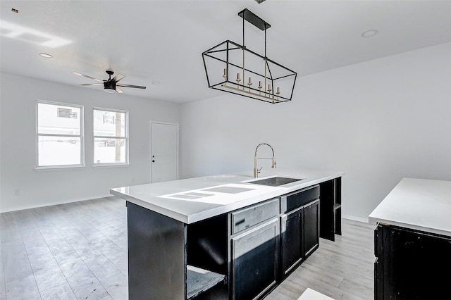 kitchen featuring a sink, ceiling fan, light countertops, and dark cabinets