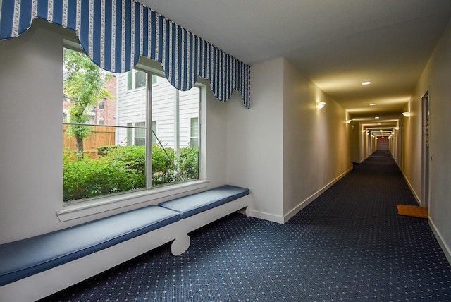 hallway featuring a wealth of natural light, dark colored carpet, baseboards, and recessed lighting