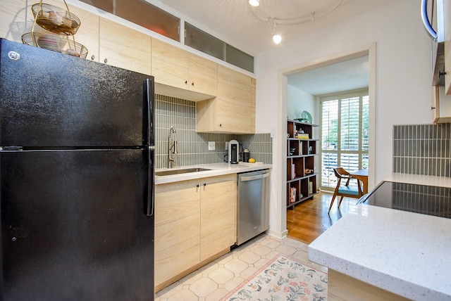 kitchen with a sink, freestanding refrigerator, stainless steel dishwasher, and light brown cabinets