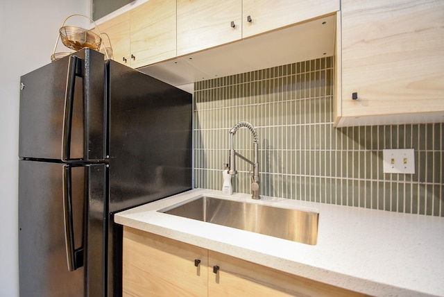 kitchen with a sink, freestanding refrigerator, light stone countertops, and decorative backsplash