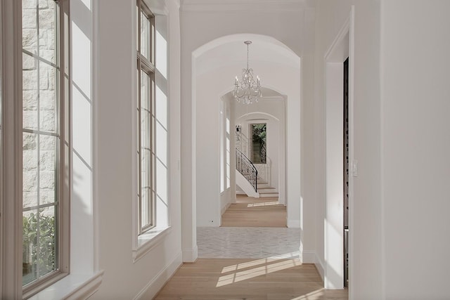 hall featuring wood finished floors, baseboards, arched walkways, and a notable chandelier