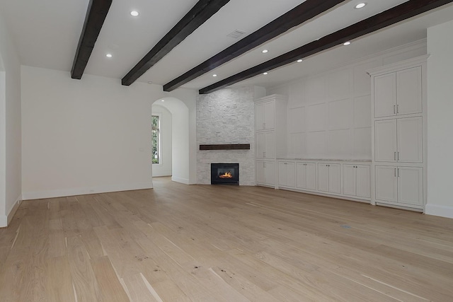 unfurnished living room with beam ceiling, light wood-type flooring, recessed lighting, arched walkways, and a stone fireplace
