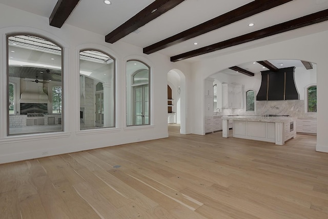 unfurnished living room with recessed lighting, light wood finished floors, a sink, arched walkways, and beam ceiling