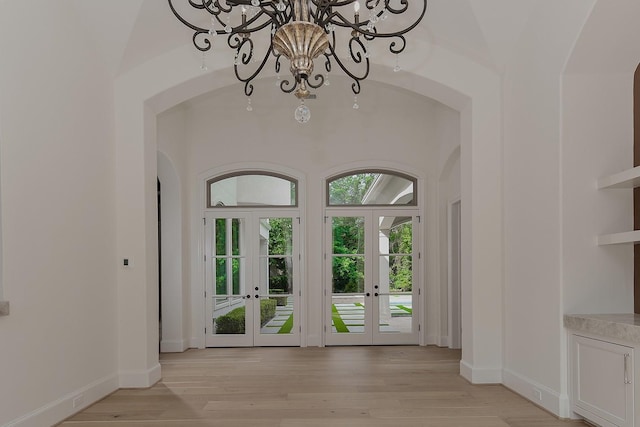 doorway with arched walkways, a notable chandelier, light wood finished floors, and french doors