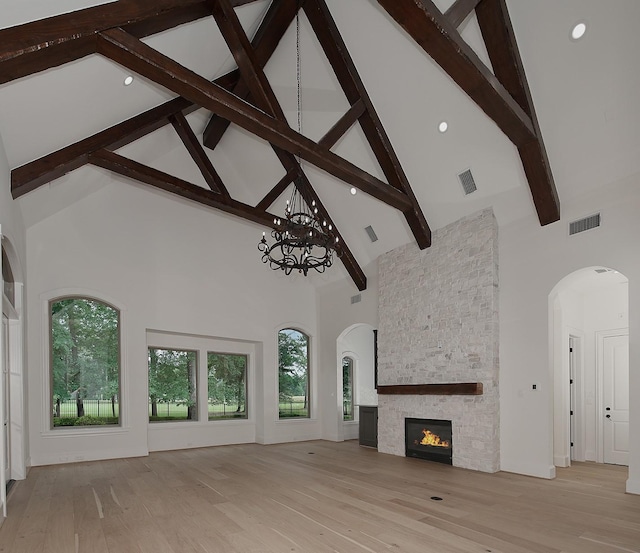 unfurnished living room featuring a stone fireplace, an inviting chandelier, visible vents, and high vaulted ceiling