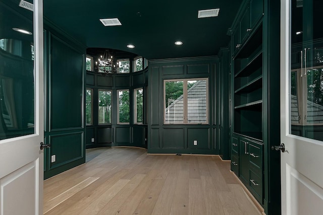 unfurnished room featuring a notable chandelier, a decorative wall, light wood-type flooring, and visible vents