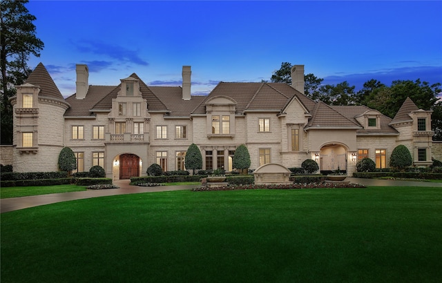 french provincial home featuring stone siding, a chimney, and a front lawn