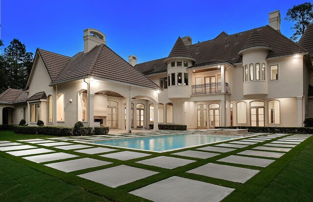 rear view of house featuring french doors, stucco siding, a chimney, a balcony, and an outdoor pool