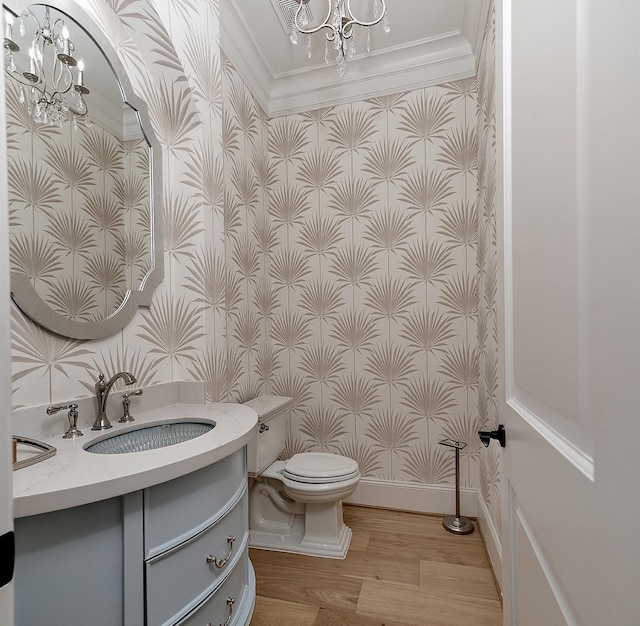 half bathroom with a chandelier, wallpapered walls, wood finished floors, toilet, and vanity