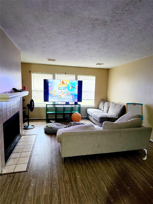 living area featuring a textured ceiling, a tile fireplace, visible vents, and wood finished floors