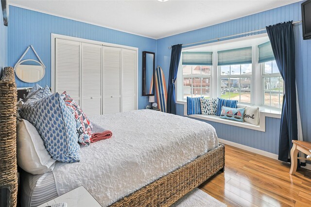bedroom with a closet, wood finished floors, baseboards, and ornamental molding