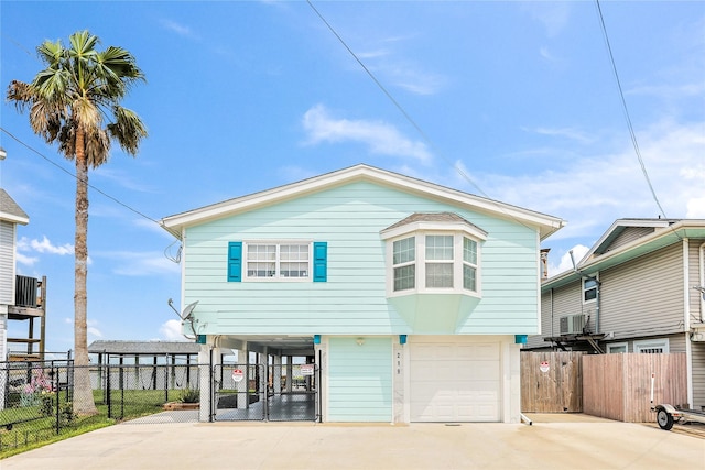 beach home featuring driveway, fence, an attached garage, central air condition unit, and a carport
