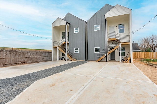 back of property featuring board and batten siding, fence, a patio, concrete driveway, and stairway