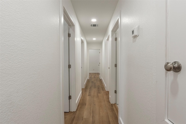 hallway with light wood-type flooring, recessed lighting, visible vents, and a textured wall