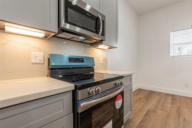 kitchen featuring light wood-style flooring, stainless steel appliances, gray cabinets, baseboards, and light stone countertops