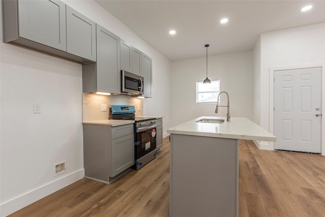 kitchen featuring a sink, gray cabinets, appliances with stainless steel finishes, a kitchen island with sink, and light wood-style floors