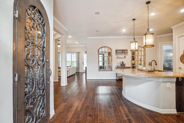 kitchen featuring a sink, dark wood finished floors, ornamental molding, light stone countertops, and baseboards