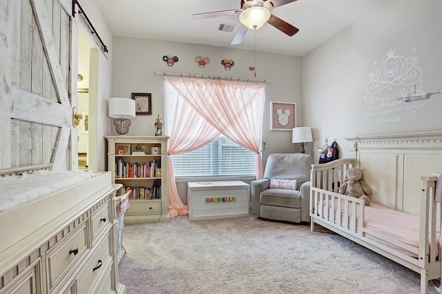 bedroom featuring light colored carpet, a crib, a barn door, and a ceiling fan