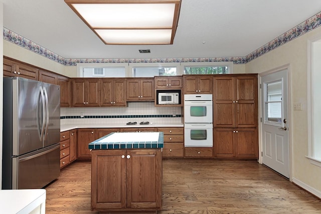 kitchen with light wood-type flooring, white appliances, a center island, and brown cabinets