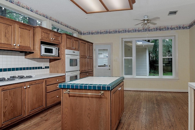 kitchen with ceiling fan, brown cabinetry, white appliances, and visible vents