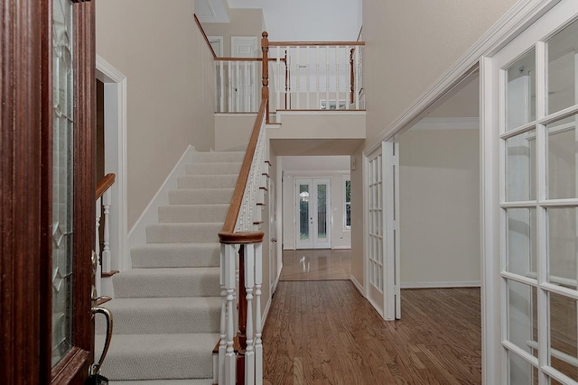 entrance foyer featuring french doors, wood finished floors, a towering ceiling, stairway, and baseboards