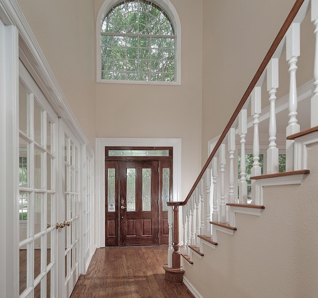 entrance foyer with french doors, wood finished floors, a towering ceiling, and stairs