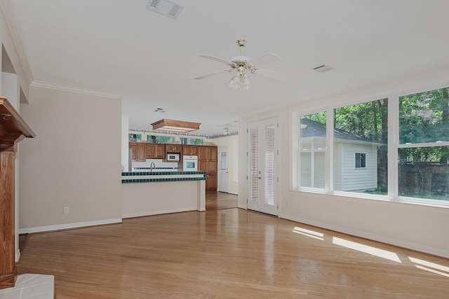 unfurnished living room with crown molding, visible vents, baseboards, ceiling fan, and light wood-style floors