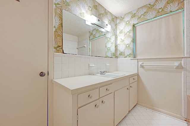 bathroom with wallpapered walls, a textured ceiling, vanity, tile patterned floors, and backsplash