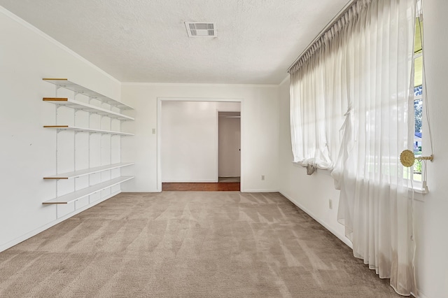 carpeted empty room featuring a textured ceiling, baseboards, and ornamental molding