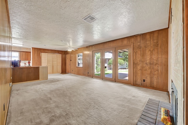 unfurnished living room featuring plenty of natural light, light carpet, a textured ceiling, wood walls, and a ceiling fan