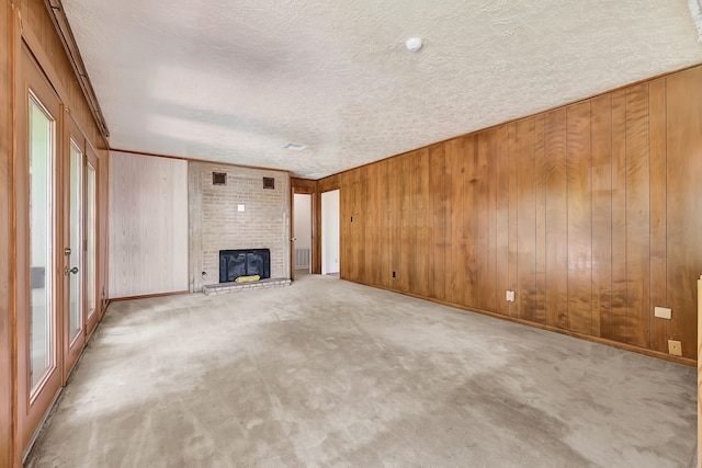 unfurnished living room featuring a textured ceiling, a brick fireplace, wooden walls, carpet floors, and baseboards
