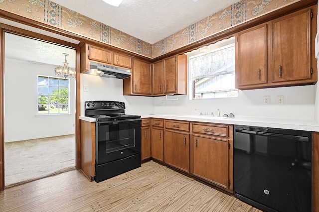 kitchen with black appliances, under cabinet range hood, a sink, light wood finished floors, and wallpapered walls