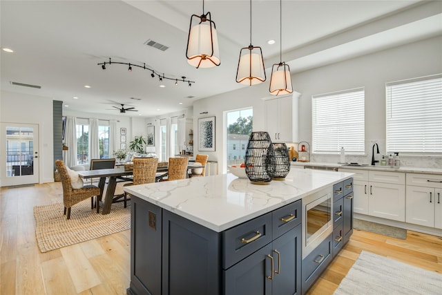 kitchen featuring stainless steel microwave, white cabinets, recessed lighting, a center island, and light wood-style floors