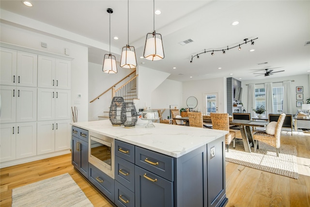 kitchen with stainless steel microwave, white cabinets, light wood-type flooring, open floor plan, and hanging light fixtures