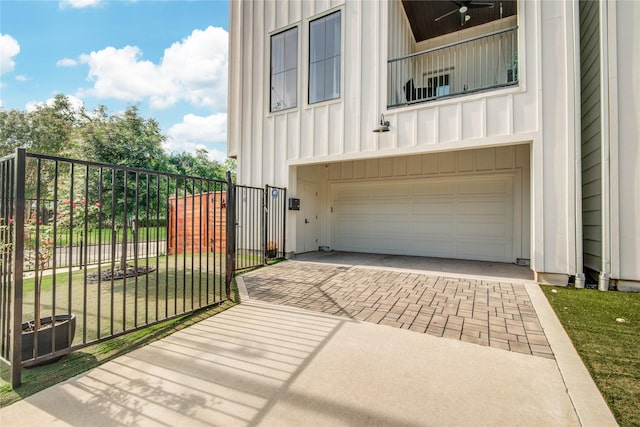 view of home's exterior featuring board and batten siding, an attached garage, decorative driveway, a balcony, and a gate