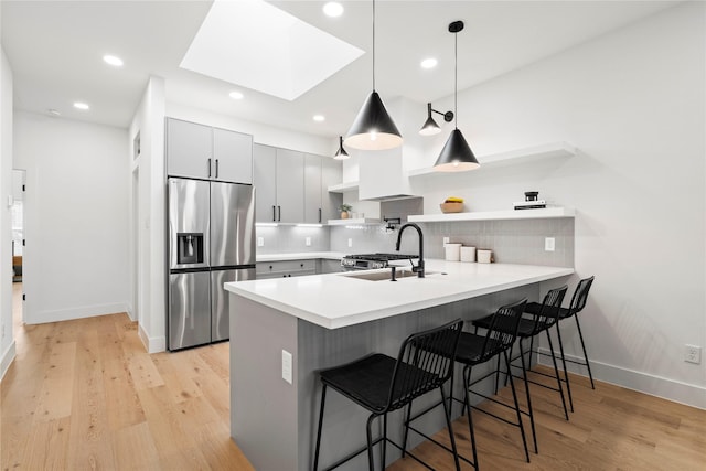 kitchen featuring a peninsula, a breakfast bar area, a sink, open shelves, and appliances with stainless steel finishes