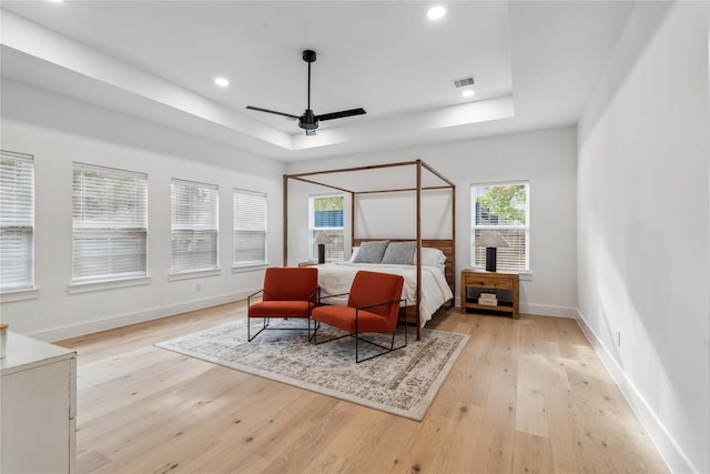 bedroom with light wood-type flooring, a raised ceiling, baseboards, and visible vents