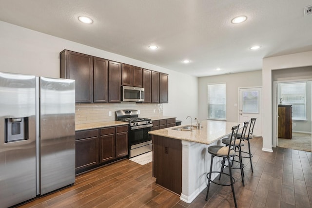 kitchen with dark brown cabinets, a kitchen bar, a sink, stainless steel appliances, and dark wood finished floors