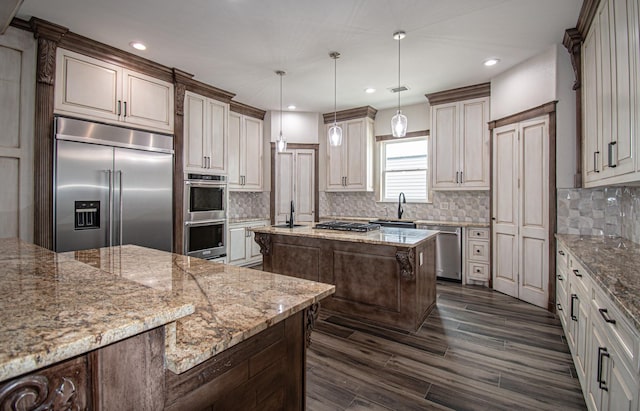 kitchen featuring light stone countertops, a center island, a sink, stainless steel appliances, and tasteful backsplash