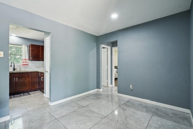 empty room featuring baseboards, light tile patterned flooring, and a sink