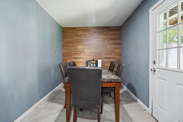 dining space featuring wooden walls, baseboards, and an accent wall