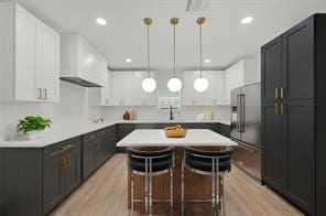 kitchen featuring high end refrigerator, light wood-style flooring, a kitchen island, custom exhaust hood, and recessed lighting