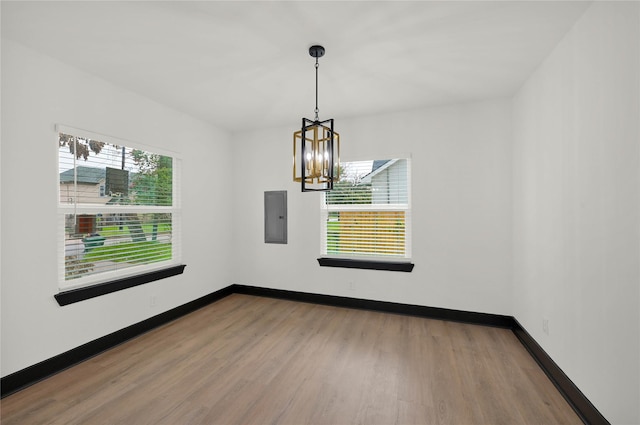 spare room with electric panel, a chandelier, wood finished floors, and baseboards