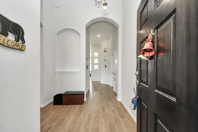 hallway featuring arched walkways, light wood finished floors, and baseboards