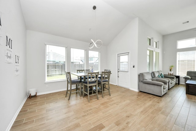 dining area with a chandelier, light wood-type flooring, baseboards, and high vaulted ceiling