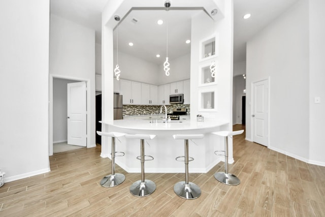 kitchen with appliances with stainless steel finishes, a breakfast bar area, light wood-style floors, a high ceiling, and recessed lighting