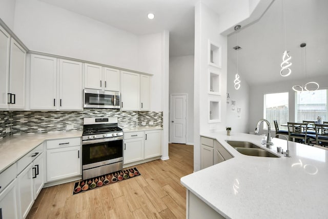 kitchen featuring stainless steel appliances, a sink, decorative backsplash, white cabinetry, and high vaulted ceiling