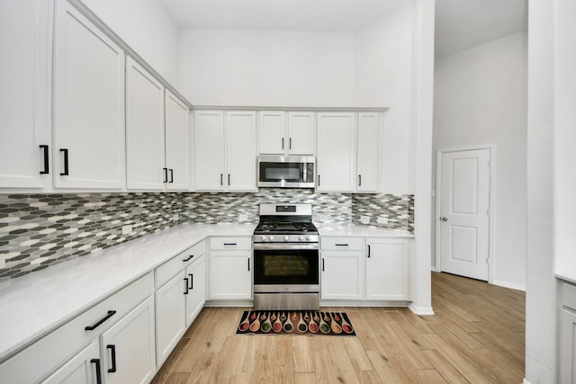 kitchen with appliances with stainless steel finishes, light countertops, light wood finished floors, backsplash, and a towering ceiling
