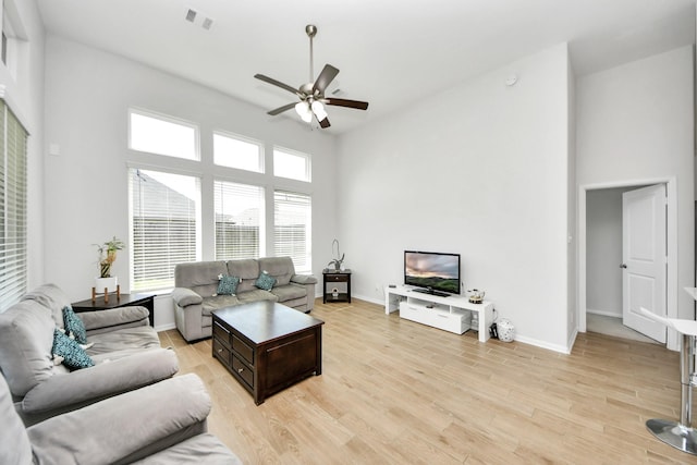 living room featuring a ceiling fan, a towering ceiling, light wood-type flooring, and baseboards