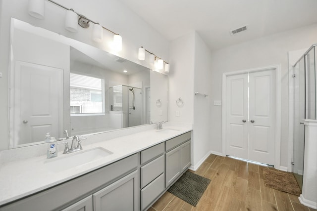 bathroom featuring a shower stall, wood finished floors, double vanity, and baseboards